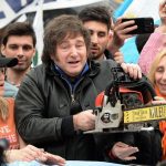 Motosierra cortando billetes de pauta oficial sobre un sillón de televisión, simbolizando el blindaje mediático del gobierno de Milei y su promesa de "corte a la casta".