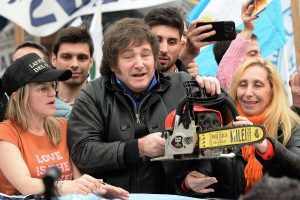 Motosierra cortando billetes de pauta oficial sobre un sillón de televisión, simbolizando el blindaje mediático del gobierno de Milei y su promesa de "corte a la casta".