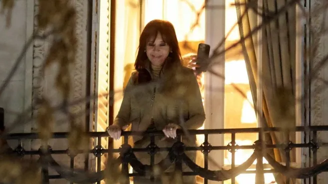 Cristina Kirchner en un balcón, hablando a una multitud, con un símbolo de boomerang en el aire, representando el efecto inverso de su condena.